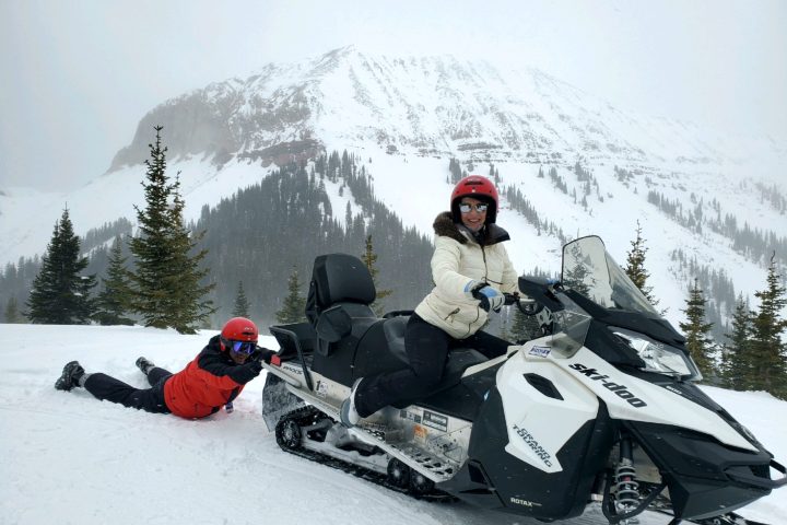 a person on a snowmobile with another person hanging onto it